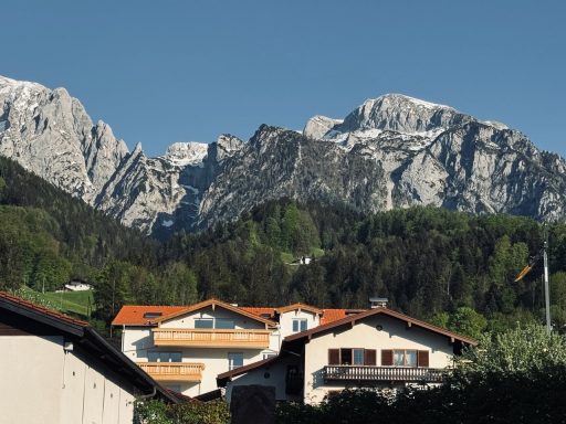 Berglandschaft mit schneebedeckten Gipfeln und bewaldeten Hängen hinter traditionellen Häusern.