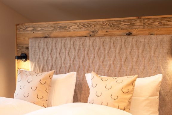 Daunenkissen laden zum Kuscheln ein Beige Kopfteil mit dekorativen Kissen und sanften Wandlampen im Hintergrund.