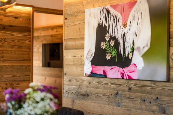 Viel Holz und warme Farben sorgen für ein Wohlfühlambiente Ein traditionelles Trachtenkleid mit Blumen und einer rosa Schleife an einer Holzwand.