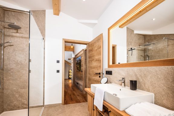 Ein Eichenschrank mit Stauraum für Ihre Kosmetika und ein großer beleuchteter Spiegel bieten weiteren Komfort Modernes Badezimmer mit Walk-In-Dusche, Waschbecken und Holzdetails.