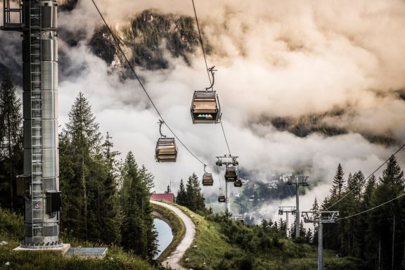 Seilbahn über grünes Gelände mit Wolken und Bergen im Hintergrund.